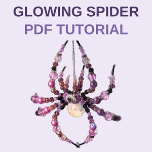May include: A spider ornament crafted from purple, pink, and black beads with a large, iridescent central bead. The text GLOWING SPIDER PDF TUTORIAL is displayed above the beaded spider, which hangs from a thin silver chain against a light background.