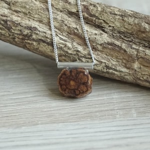 Può includere: Una collana con catena d'argento con un ciondolo in legno marrone con un design floreale dettagliato. Il ciondolo è attaccato alla catena con una barra d'argento.