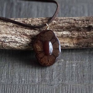 May include: A brown leather cord necklace with a pendant featuring a carved wooden flower with a red gemstone in the center.