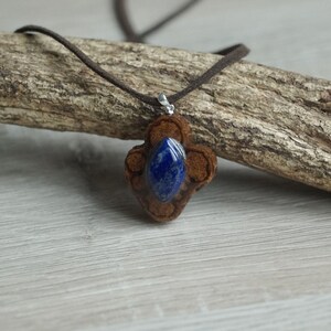 Può includere: Un ciondolo in lapislazzuli blu incastonato in una cornice di legno con un cordoncino in pelle marrone.