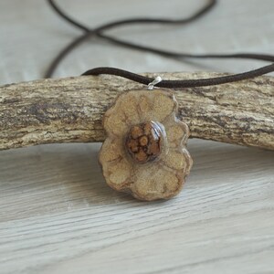 Può includere: Un ciondolo a forma di fiore in ceramica marrone con un centro maculato marrone e bianco. Il ciondolo è appeso a un cordoncino marrone.