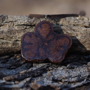 Può includere: Una collana con un ciondolo a forma di fiore marrone e nero con un cordoncino in pelle marrone.