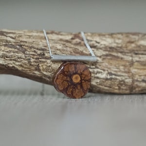 Può includere: Una collana con catena d'argento con un ciondolo in legno marrone con un motivo floreale. Il ciondolo è attaccato a una barra d'argento.