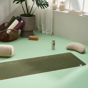 May include: A green yoga mat with a textured surface, a brown yoga block, a white yoga bolster, a silver water bottle, and a white crescent-shaped yoga cushion.