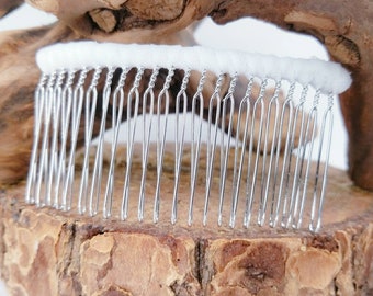 May include: A silver hair comb with a white fabric base. The comb has a row of small, closely spaced teeth.