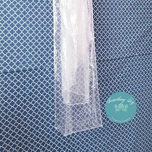 May include: A clear plastic garment bag with a hanger, hanging against a blue and white patterned background. The bag is designed to protect and store clothing.