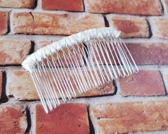 May include: A white satin ribbon wrapped around a silver hair comb. The comb has a row of teeth that are evenly spaced.