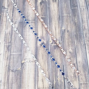 Pu&ograve; includere: Tre braccialetti in argento e oro rosa con pietre blu e trasparenti. I braccialetti sono su uno sfondo di legno.