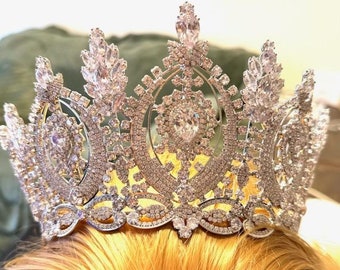 May include: A silver crown with a large, clear crystal in the center and smaller crystals surrounding it. The crown has a delicate, intricate design and is adorned with many sparkling crystals.