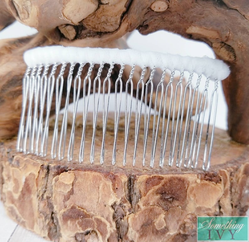 May include: A silver hair comb with a white fabric base. The comb has a row of small, closely spaced teeth.