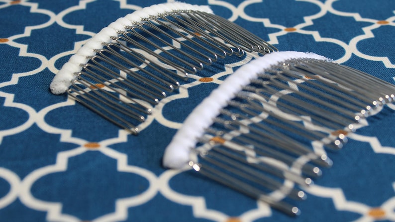 May include: Two silver hair combs with white cushioned grips. The combs are on a blue and white patterned fabric.
