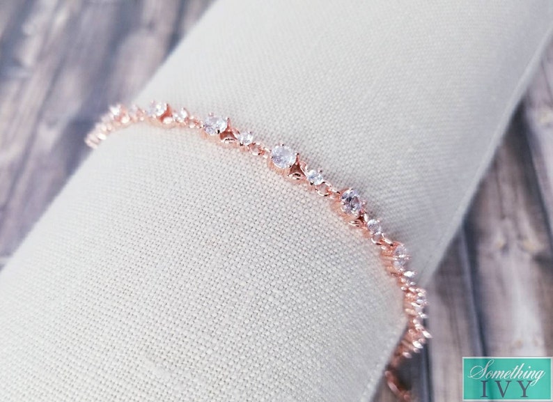 Pu&ograve; includere: Un delicato braccialetto in oro rosa con una fila scintillante di pietre di zircone cubico trasparenti. Il braccialetto ha un design delicato e femminile.