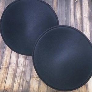 Puede incluir: Dos almohadillas redondas de fieltro negro, una ligeramente más grande que la otra, sobre una superficie de madera.