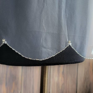 May include: White bridal veil with a scalloped edge and silver glitter trim. The veil is displayed on a black mannequin.