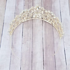 Puede incluir: Tiara plateada con un dise&ntilde;o calado ornamentado. La corona presenta una serie de adornos brillantes y una banda delicada y curvada. La tiara est&aacute; dise&ntilde;ada para eventos formales y ocasiones especiales.