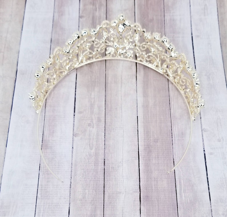 Puede incluir: Tiara plateada con un dise&ntilde;o calado ornamentado. La corona presenta una serie de adornos brillantes y una banda delicada y curvada. La tiara est&aacute; dise&ntilde;ada para eventos formales y ocasiones especiales.
