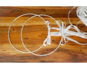 May include: Two silver wedding crowns with white satin ribbon tied together. The crowns are decorated with small white beads.