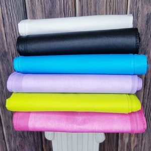 Pode incluir: Uma pilha de seis toalhas de mesa de tecido em várias cores, incluindo branco, preto, azul claro, lavanda, verde limão e rosa. As toalhas de mesa estão dobradas e empilhadas umas sobre as outras.