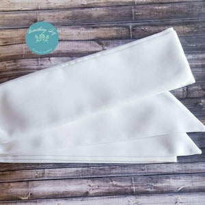 May include: White satin ribbon sash, folded in thirds, with a subtle sheen. The sash is approximately 2.5 inches wide and is perfect for adding a touch of elegance to any occasion.