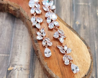 May include: A pair of rose gold dangle earrings with clear crystal stones in a floral design.