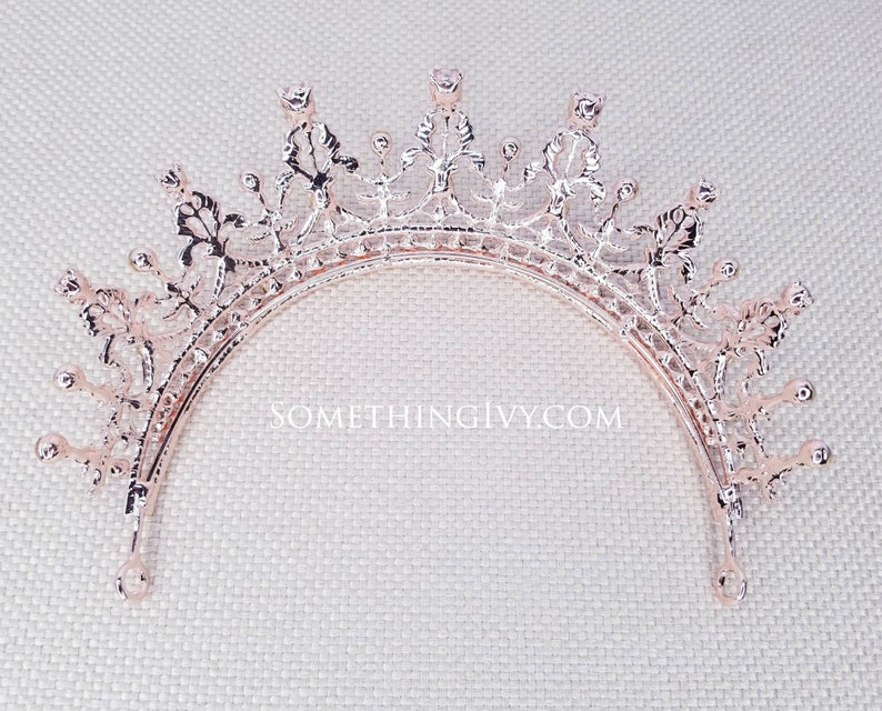 Puede incluir: Tiara de oro rosa con un delicado dise&ntilde;o floral y brillantes transparentes. La tiara es curva y tiene una parte superior puntiaguda.