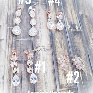 Puede incluir: Un conjunto de seis pares de pendientes de oro rosa con piedras de cristal transparentes. Los pendientes est&aacute;n numerados del 1 al 4. Los pendientes n.&ordm; 1 y n.&ordm; 2 son pendientes colgantes. Los pendientes n.&ordm; 3 y n.&ordm; 4 son pendientes de gota. El texto "Earring Upgrade" est&aacute; en la parte inferior de la imagen.