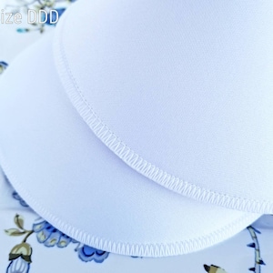 Könnte beinhalten: Zwei weiße Stoff-Stillkissen mit einem genähten Rand. Die Kissen liegen übereinander. Der Text "Größe DDD" ist in der oberen linken Ecke des Bildes sichtbar.