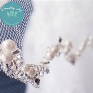 May include: Close-up of a white bridal veil with a beaded trim. The trim features small pearls and rhinestones.