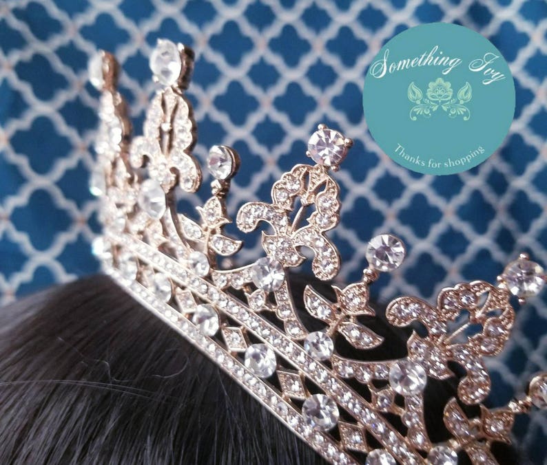 Puede incluir: Una corona dorada con brillantes transparentes. La corona tiene una punta puntiaguda y un dise&ntilde;o decorativo con motivos de flor de lis.