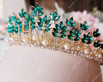 May include: A gold tiara with emerald green and clear rhinestones, and pearl accents. The tiara has a leaf design.