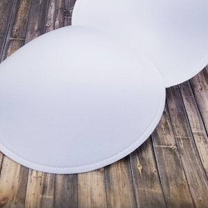 May include: Two white, round, fabric bra inserts on a wooden surface.