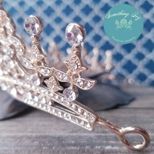 Puede incluir: Una tiara dorada con brillantes transparentes y un bucle en la parte posterior para sujetarla al cabello.