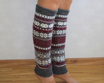 May include: Gray and white knitted leg warmers with a red geometric pattern. The leg warmers are worn on a person's legs.
