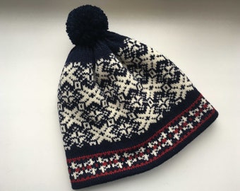 May include: A navy blue knit beanie with a white and red geometric pattern and a fluffy pom pom on top.