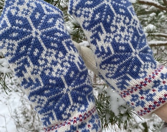 May include: A pair of white knitted mittens with a blue and white snowflake pattern. The mittens have a red and blue trim at the cuff.