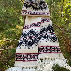 May include: White knitted hat and scarf set with a black and red geometric pattern. The hat has a white pompom on top.