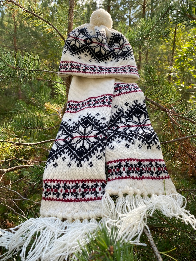 May include: White knitted hat and scarf set with a black and red geometric pattern. The hat has a white pompom on top.