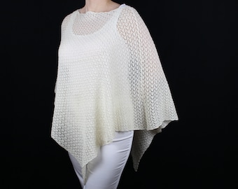 Può includere: Un poncho bianco all'uncinetto con un delicato motivo traforato. Il poncho ha una forma triangolare e un'ampia scollatura.