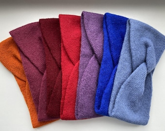 Könnte beinhalten: Eine Sammlung von sechs gestrickten Stirnbändern, die fächerförmig angeordnet sind und ein gedrehtes Design auf der Vorderseite aufweisen. Die Farben umfassen Orange, Dunkelmagenta, Dunkelrot, Hellrot, Lila, Königsblau und Hellblau aus Strick.