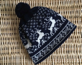May include: A navy blue knit beanie with a white reindeer pattern and a fluffy pom pom on top.