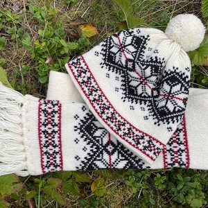 May include: White knitted hat and scarf set with a black and red geometric pattern. The hat has a white pompom on top.