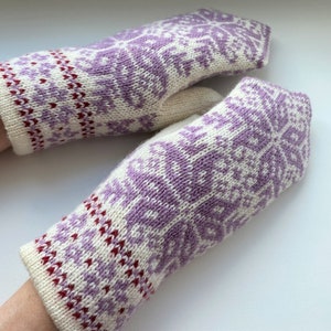 Puede incluir: Un par de guantes tejidos con fondo blanco y un patrón de copo de nieve morado y rojo.