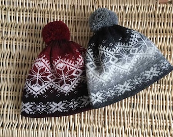 May include: Two knitted winter hats with pom poms. One hat is red and black with a white snowflake pattern, the other is gray and black with a white snowflake pattern.