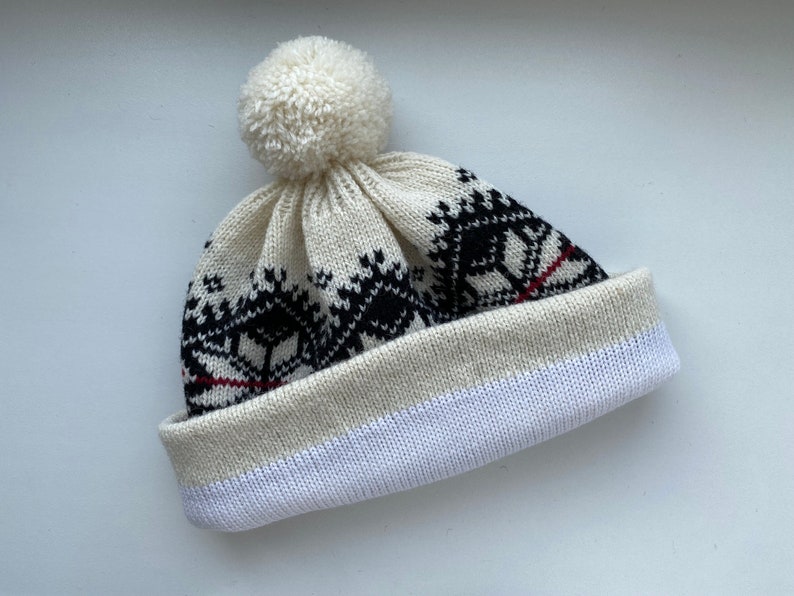 May include: White knit beanie with a black and red geometric pattern and a white pom pom on top.
