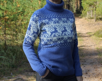 May include: A blue turtleneck sweater featuring a cream-colored knit pattern of reindeer and snowflakes across the chest and shoulders. The long-sleeved garment has a ribbed collar, cuffs, and hem, with a solid blue lower section and sleeves.