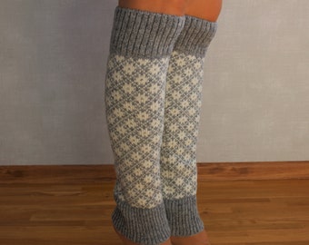 May include: A pair of gray and white patterned leg warmers. The leg warmers have a ribbed gray cuff at the top and bottom, with a diamond pattern in white and gray covering the leg. The background is a light gray wall and a wooden floor.