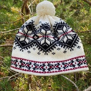May include: White knitted hat with a black and red geometric pattern and a white pom pom on top.