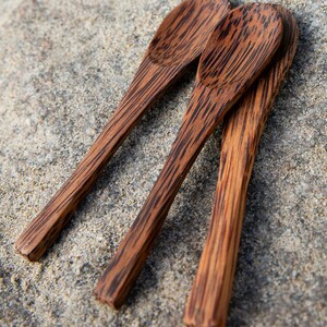 May include: Three wooden spoons made from coconut wood. The spoons are brown with dark brown stripes. The spoons are arranged in a triangle shape.