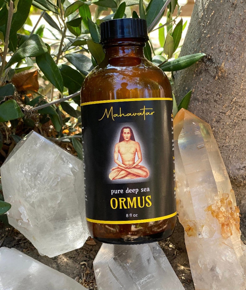 May include: A brown glass bottle with a black cap, labeled "Mahavatar pure deep sea ORMUS 8 fl oz". The bottle is sitting on a white crystal.