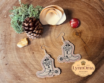 May include: A pair of brown leather earrings with a black embroidered cowboy boot design. The earrings are hanging from silver hooks. The earrings are labeled "LynnOma Designs" with the text "Est. 2016".